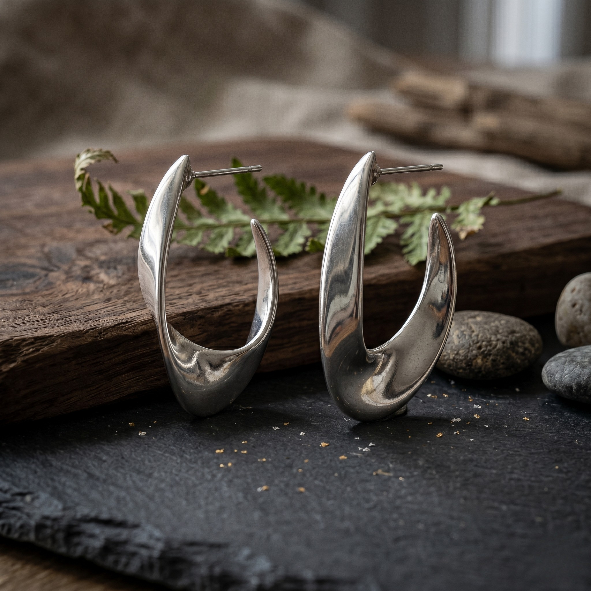 Detailed close-up of the Luna Curve sterling silver jewelry hoops in a bright rhodium plated finish, highlighting the sculptural shape and high-polish surface of these contemporary silver earrings.