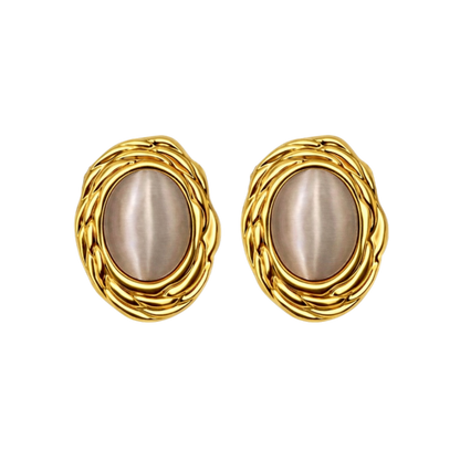 The Gia stud earrings styled on a model, showcasing how the 18k gold plated stainless steel frame and luminous cat’s eye stone catch the light against the skin. The vintage texture and elegant oval shape highlight the luxurious presence of these statement stud earrings when worn.