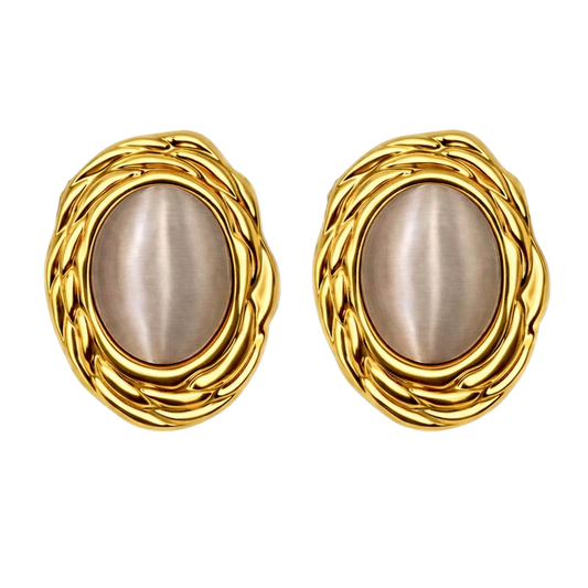 The Gia stud earrings styled on a model, showcasing how the 18k gold plated stainless steel frame and luminous cat’s eye stone catch the light against the skin. The vintage texture and elegant oval shape highlight the luxurious presence of these statement stud earrings when worn.